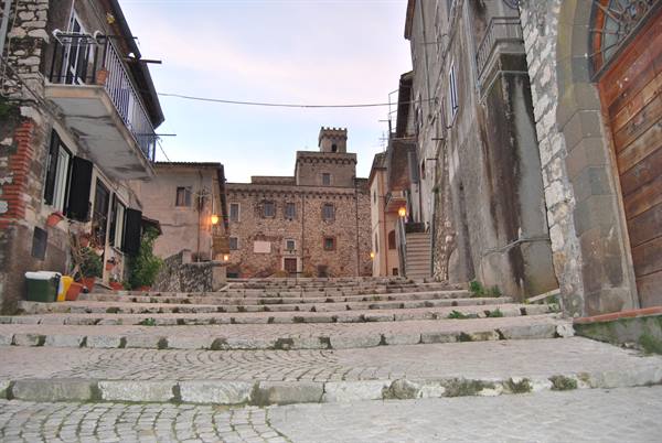 Stone stairway between old houses toward a turreted building, warm evening lights