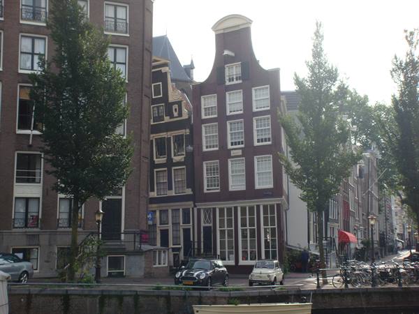 Curved-gabled brick facade along Amsterdam canal, parked cars and bicycles below