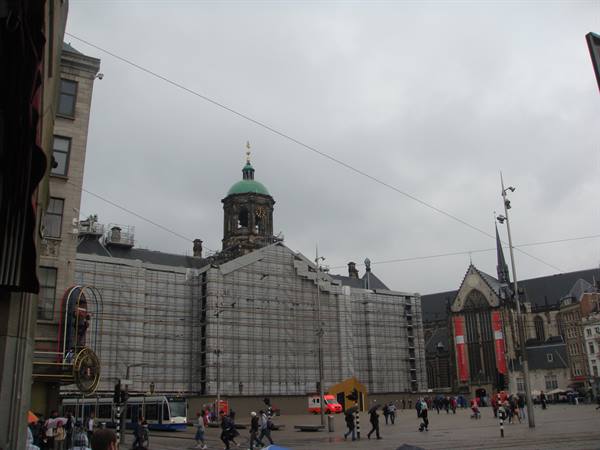 The Royal Palace wrapped in scaffolding at Dam square, pedestrians and tram under grey sky