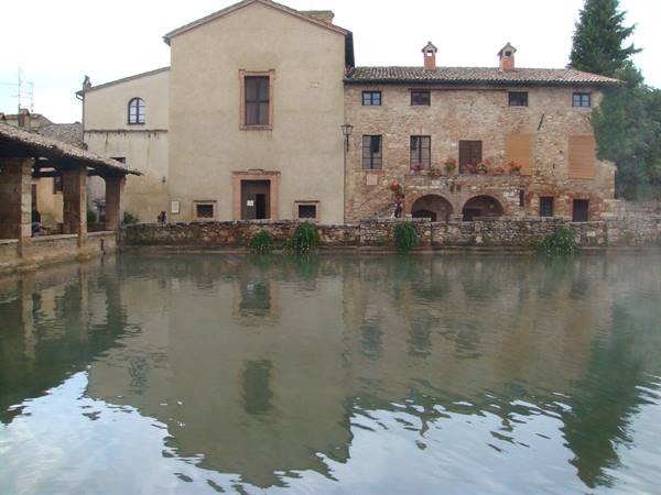 Bagno Vignoni: stone and brick buildings reflected in the thermal pool, grey light