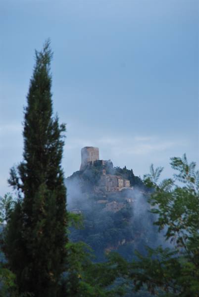 Cypress and trees frame the hilltop fortress wrapped in morning mist