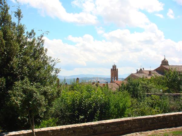 Stone wall, terracotta rooftops and bell tower among green trees and hills