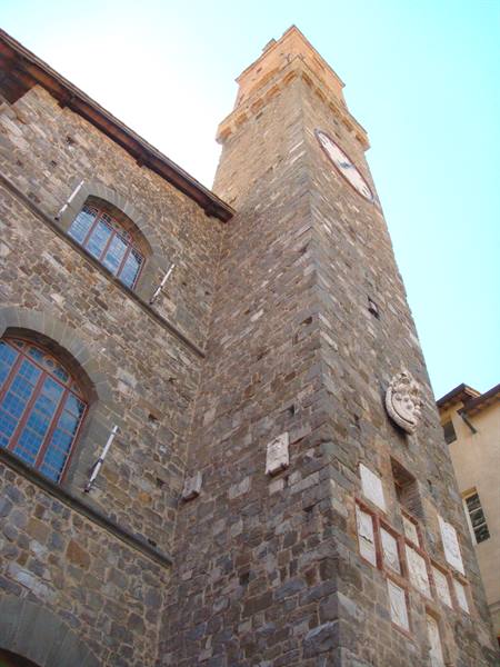 Pienza: stone civic tower with clock against the blue sky