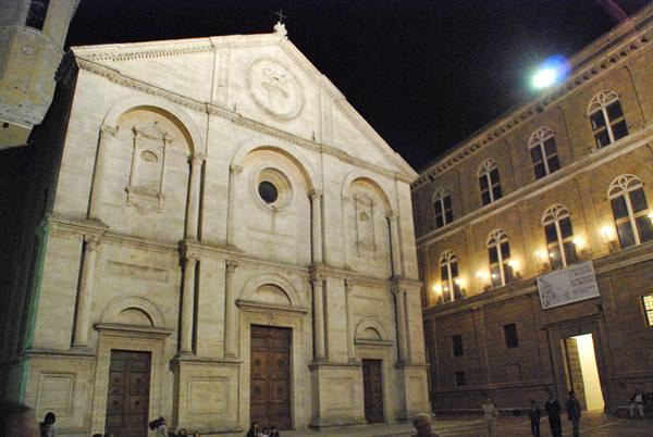 Pienza Cathedral at night, illuminated travertine facade beside a lit palazzo
