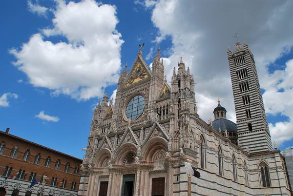 Marble Gothic facade of Siena Cathedral with striped bell tower under white clouds
