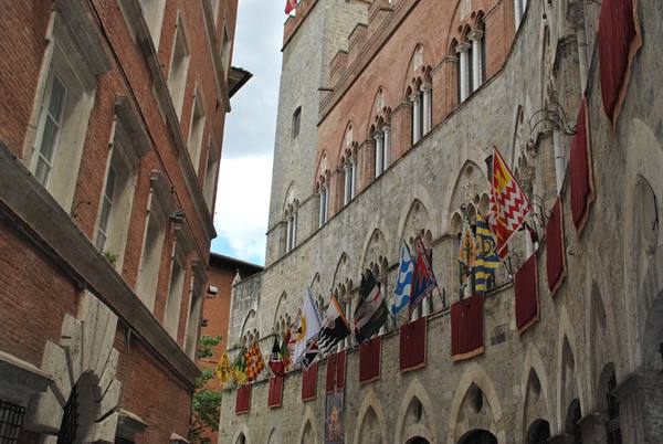 Siena, Palazzo Pubblico with contrade flags under a cloudy sky