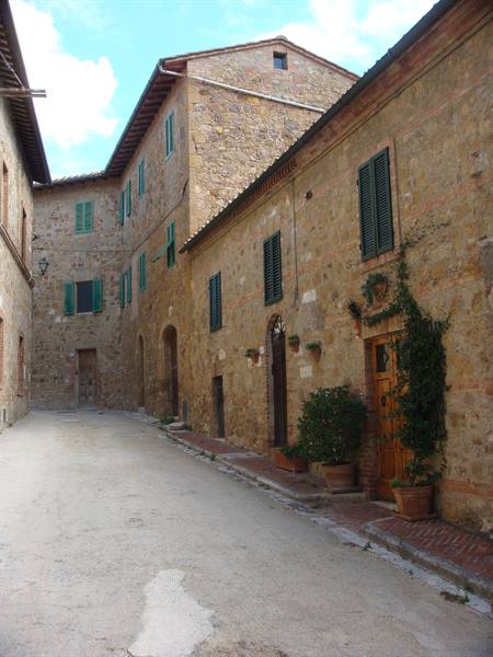 Stone alley with medieval houses and green shutters in San Quirico d'Orcia