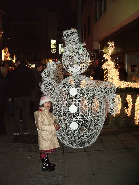 Little girl next to a glowing wire snowman at a Christmas market