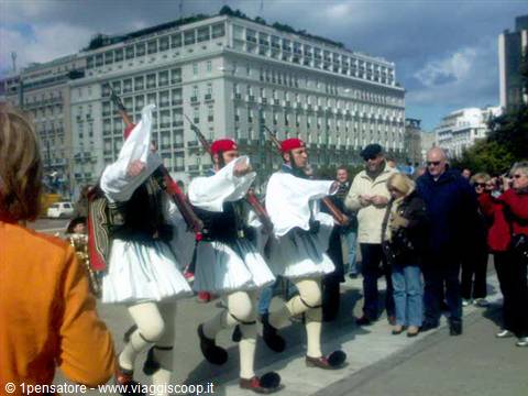 Evzones in fustanella march with rifles past tourists in the city