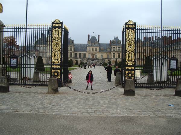 Child in front of gilded iron gates of Fontainebleau castle, gray sky