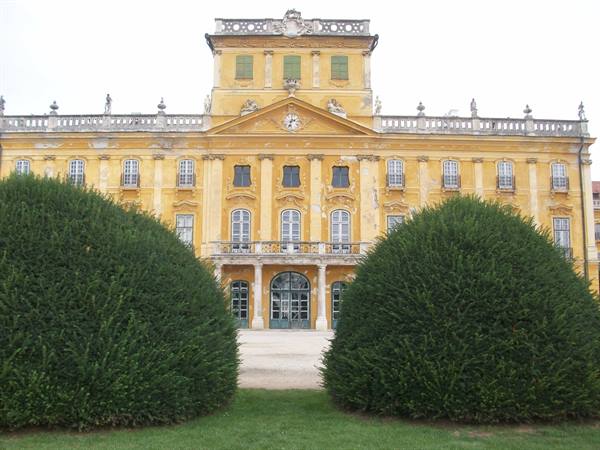 Esterházy Palace in Fertőd, yellow facade with clock, rounded hedges on lawn