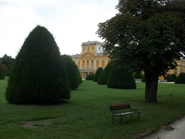 Wooden bench and clipped conifers in front of the yellow Esterházy palace in Fertőd