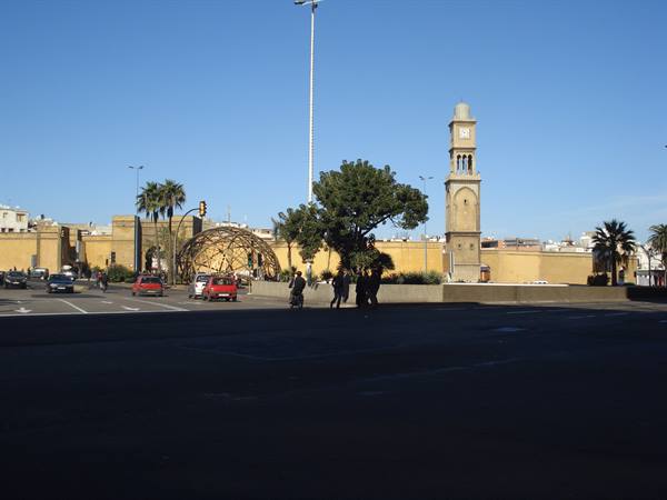 Clock tower beside ochre walls, palm trees and cars along the road