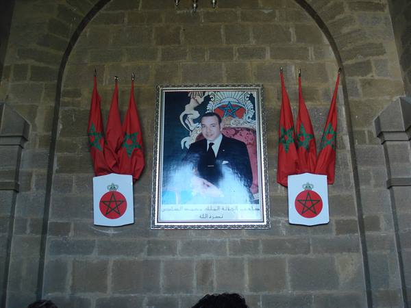 Framed portrait of King Mohammed VI on stone wall with red Moroccan flags