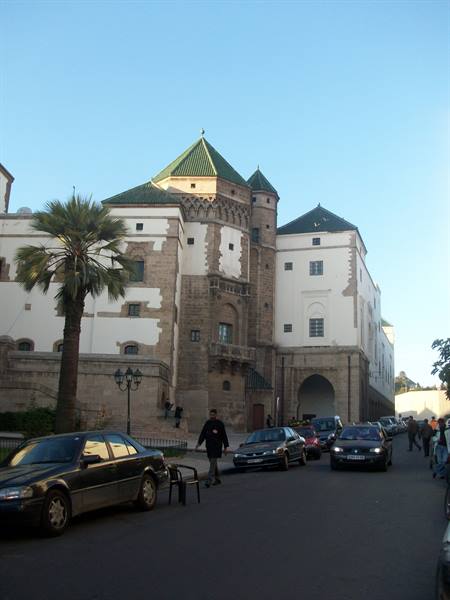 White building with green tiled roofs and stone tower, palms and parked cars, Casbah of Algiers