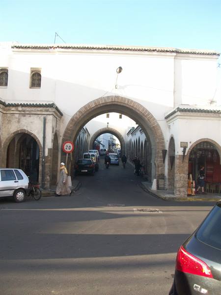 Stone arched gate over a street with cars and pedestrians in Essaouira medina