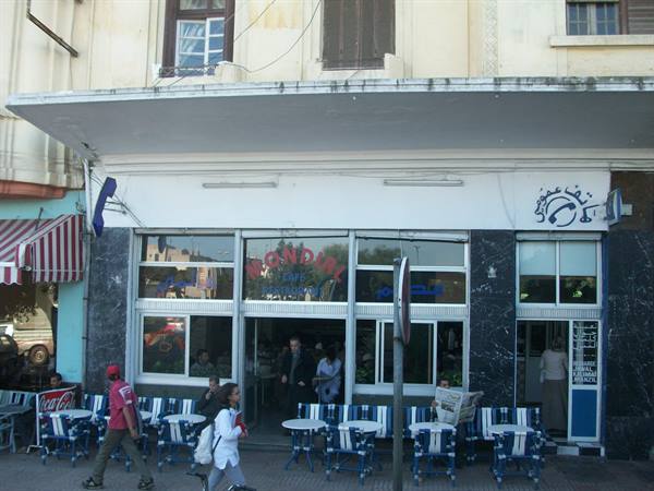 People walk past the Mondial cafe with blue and white striped chairs