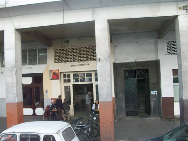 Man sitting outside a café under a colonnade, with bicycles and a white car parked