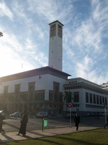 White minaret above the mosque, pedestrians crossing the street in morning light