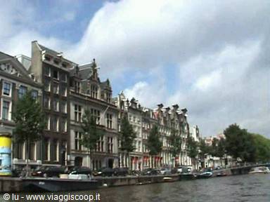 Brick facades along Amsterdam canal, moored boats, cloudy sky