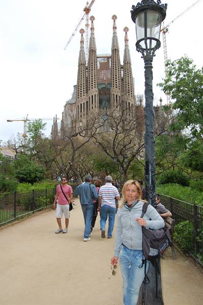 Woman with backpack leaning on a lamppost, Sagrada Familia under construction behind