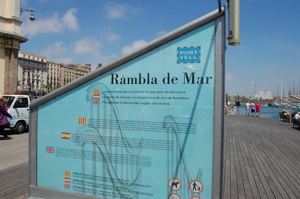 Information sign of Rambla de Mar at Port Vell, wooden walkway and buildings