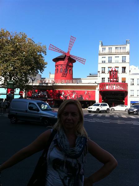 Blonde woman in front of the Moulin Rouge windmill in Paris, blue sky