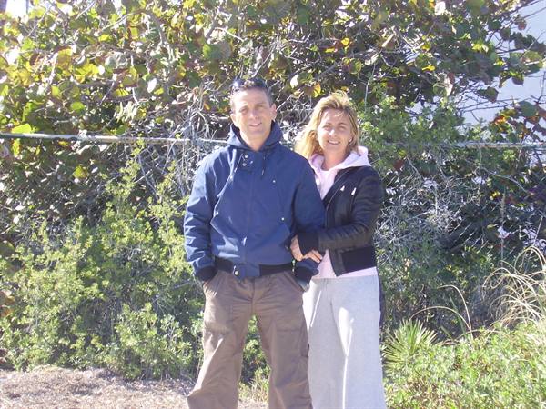 Couple in jackets arm in arm before green bushes in sunlight