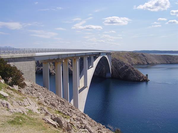 Concrete arch bridge spanning the blue Adriatic among rocky arid shores