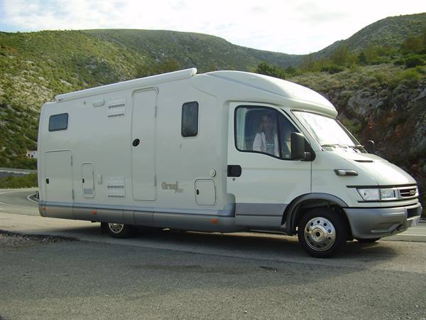 White Iveco motorhome parked on asphalt road among green hills