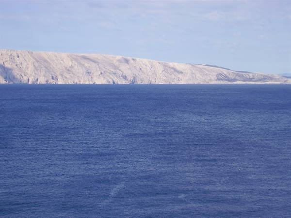 Rocky limestone coastline on the horizon across the blue sea, Pag island