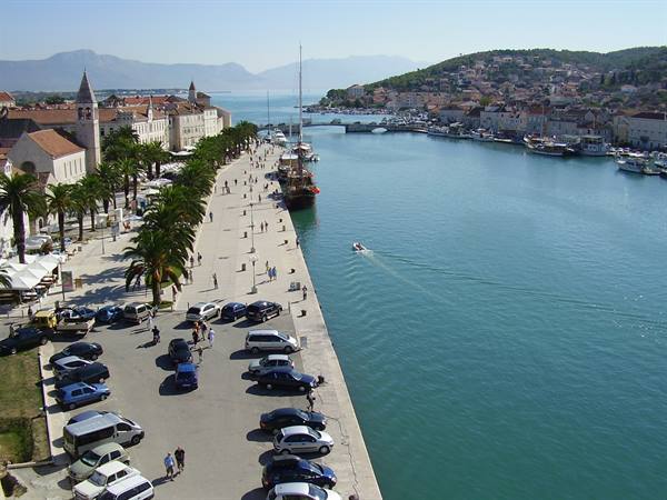 Palm-lined waterfront in Trogir, boats moored, people strolling in sunshine