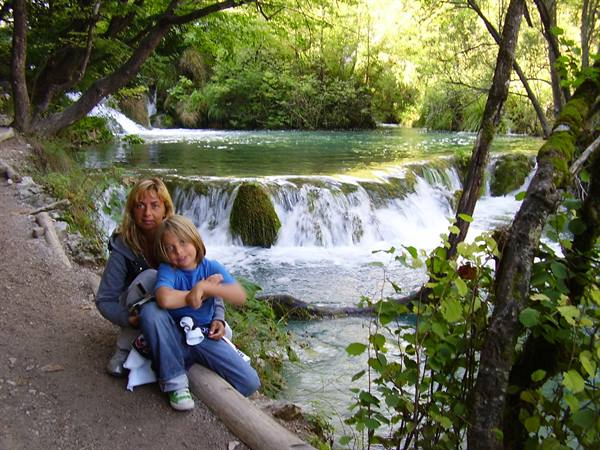 Mother and child sitting on a log in front of Plitvice waterfalls