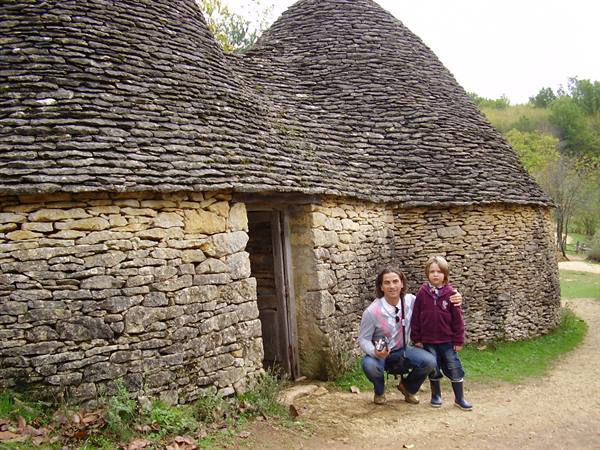 Mother and daughter crouching in front of dry-stone huts with conical roofs