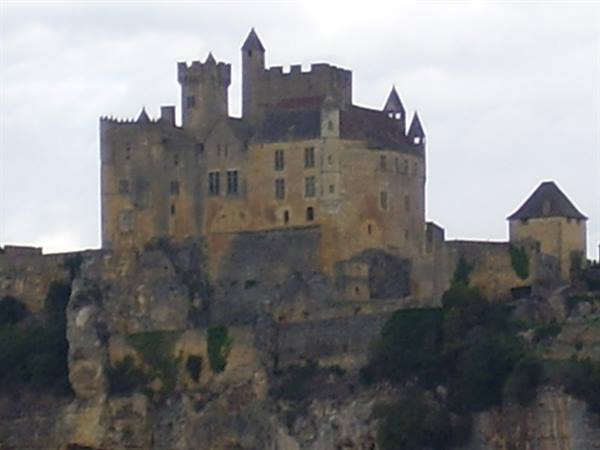 Beynac stone castle with towers perched on cliff under grey sky