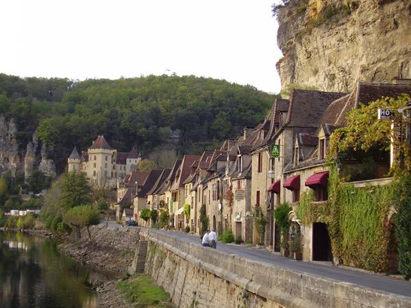 Stone houses beneath the cliff in La Roque-Gageac, river and castle in background