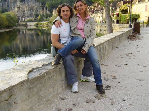 Smiling couple sitting on a stone wall along the river in La Roque-Gageac