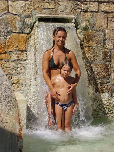 Woman and child bathing under Saturnia thermal waterfall, warm water over stone wall