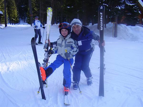 Ski instructor and child in blue suits holding Völkl skis on snow