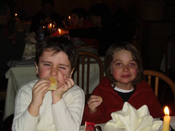 Two children eating bread at a candlelit restaurant table