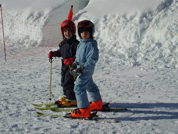 Two kids in helmets on skis by the orange safety net