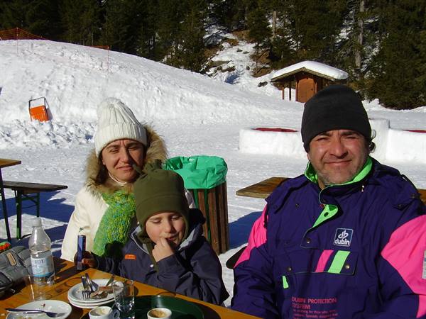 Family in wool hats sitting at an outdoor table on snowy mountain