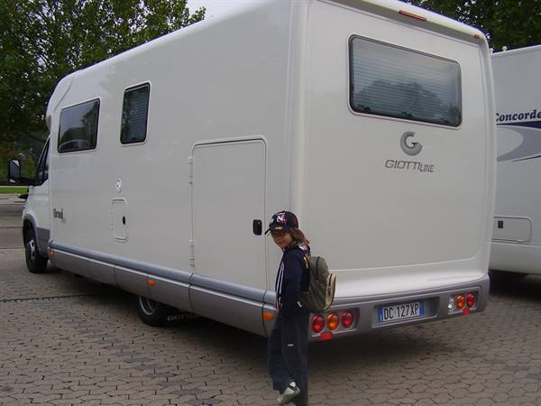 Kid with cap and backpack next to a white GiottiLine motorhome parked