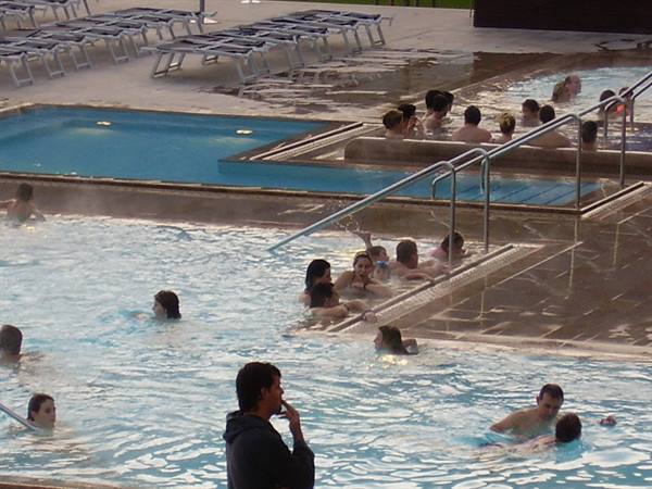People bathing in outdoor thermal pool, sun loungers and handrails nearby