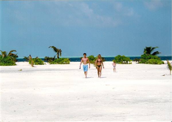 Couple and child walking on white sand between bushes and palm trees