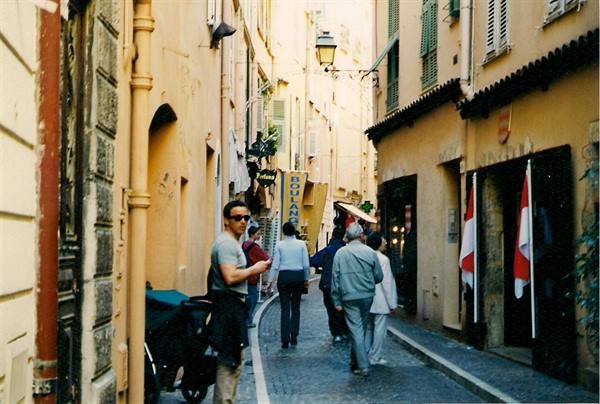 Tourists walk through a cobbled alley between ochre buildings, red and white flags