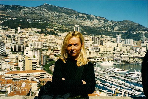 Blonde woman in black in front of Monaco harbor with yachts and mountain