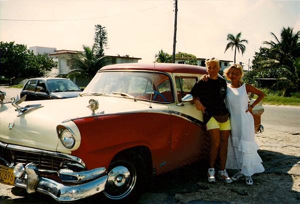 Couple beside a vintage red and white car on a tropical road
