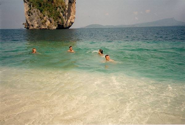 Four friends swimming in turquoise water in front of a limestone karst