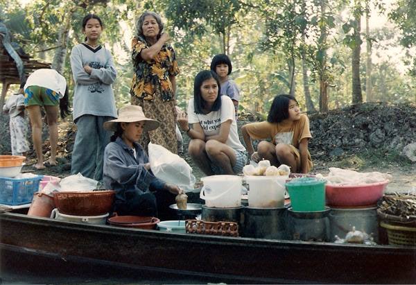 Women with buckets and baskets on a river boat, tropical forest behind